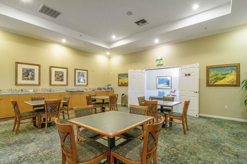 A room with a table and chairs in the foreground and a framed painting on the wall.
